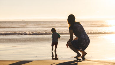 Woman Crouching Behind Son Running On Shore