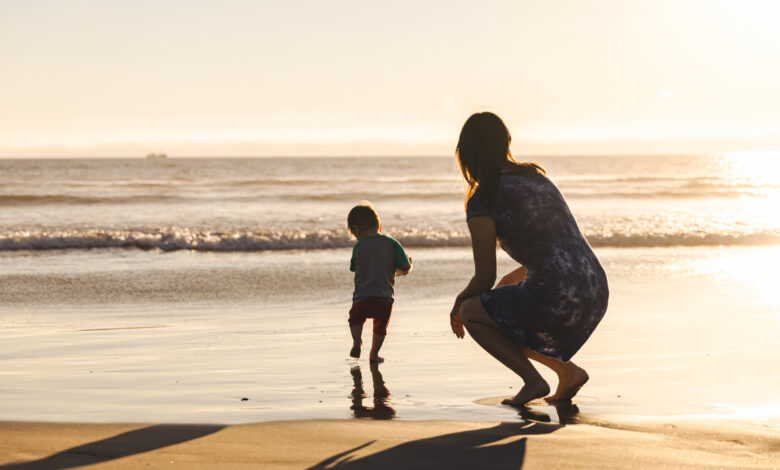 Woman Crouching Behind Son Running On Shore