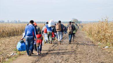 Refugees and migrants walking on fields. Group of refugees from