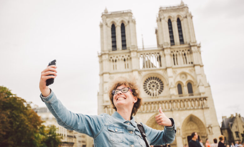 Tourist in Paris making funny selfie near Notre Dame Cathedral. Beautiful young Caucasian tourist woman with backpack in Paris making funny selfie hand holding phone, photo near Notre Dame Cathedral