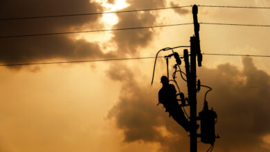 The silhouette of power lineman climbing on an electric pole wit