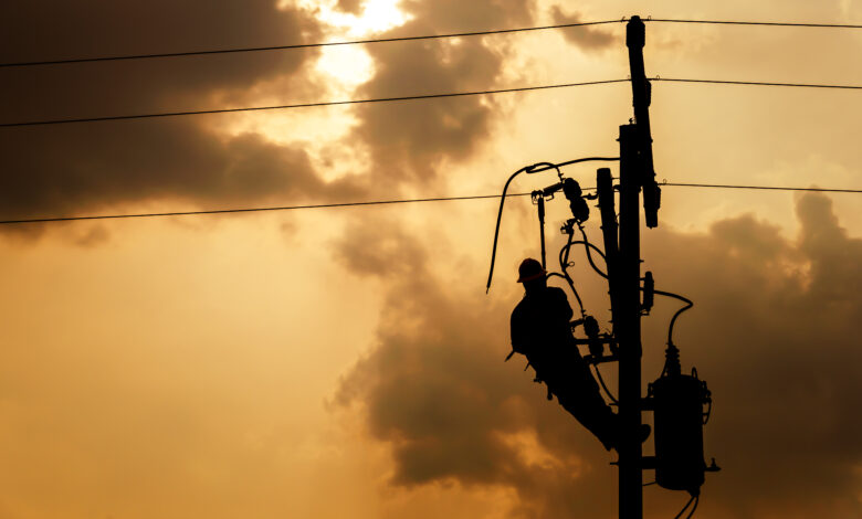 The silhouette of power lineman climbing on an electric pole wit