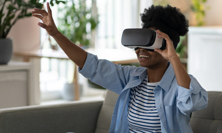 Happy excited young black woman enjoying virtual reality shopping experience while resting at home