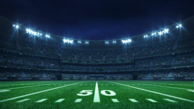 American football league stadium with white lines and fans, illuminated field side view at night